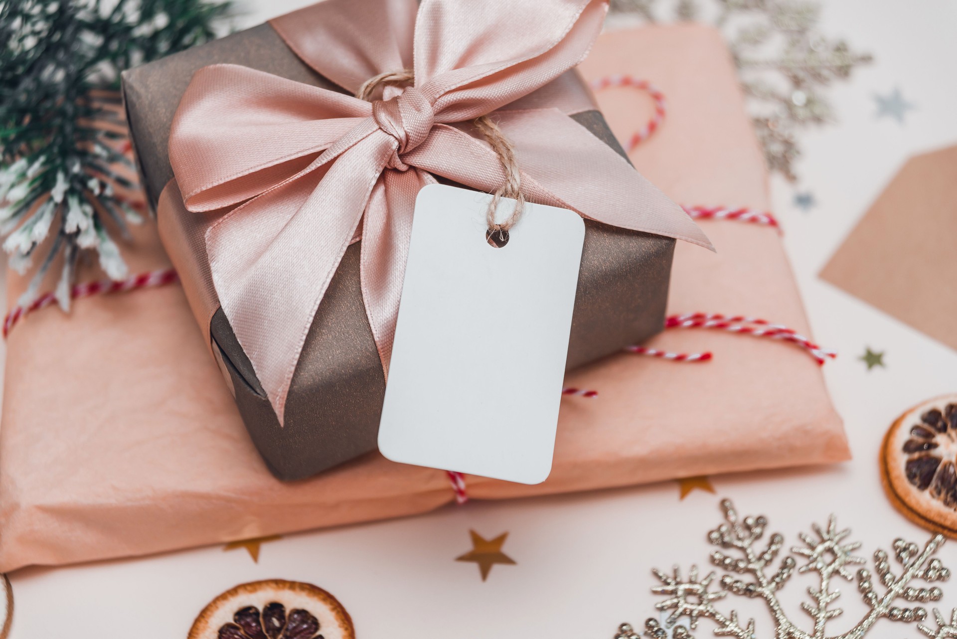 Gift box wrapped in craft paper with perfect pink ribbon and empty tag. Mockup. Festive Christmas concept.